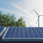 Solarpanel mit Windrädern und Baumkronen vor einem leicht wolkigen Himmel im Hintergrund