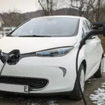 Ein weißes Elektroauto steht im Winter an der ladesäule eines Hauses und wird aufgeladen.
